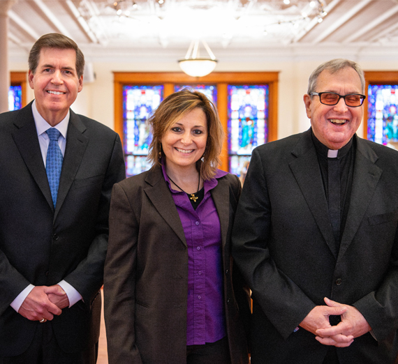 A woman in graduation cap and gown smiles at the camera